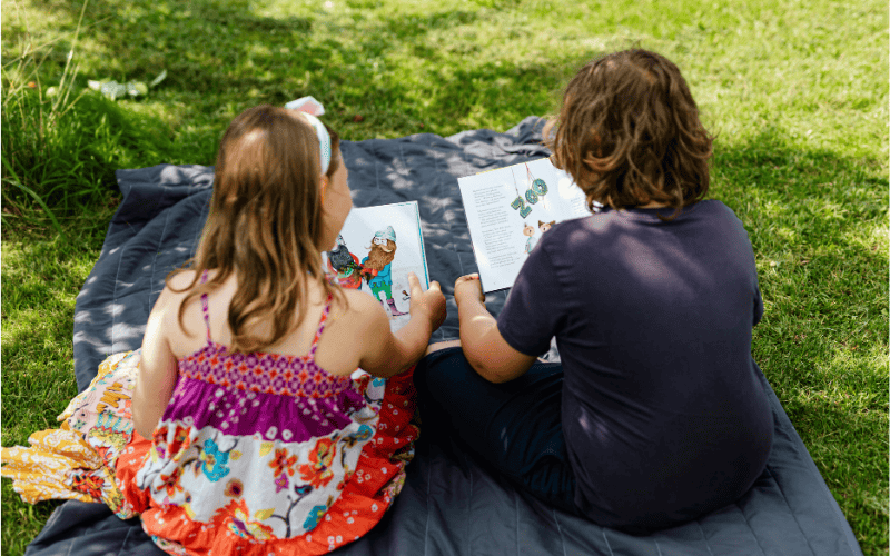 Two children reading books together in the grass